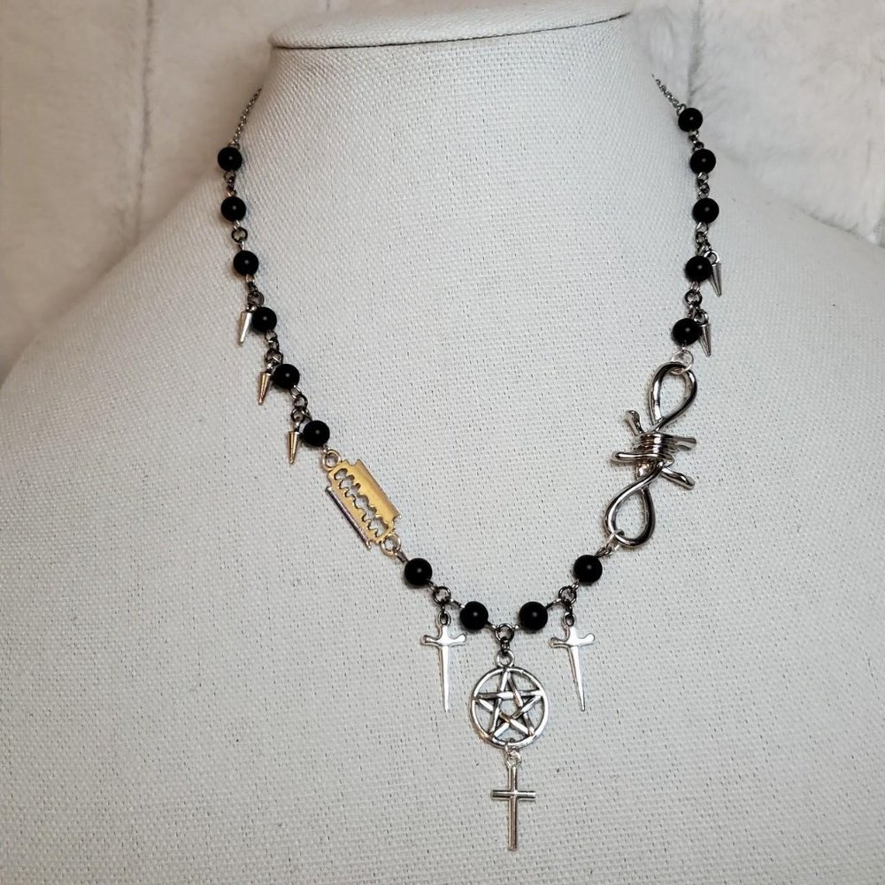 Pentagram necklace with daggers, cross, barbed wire and razor blade charms.